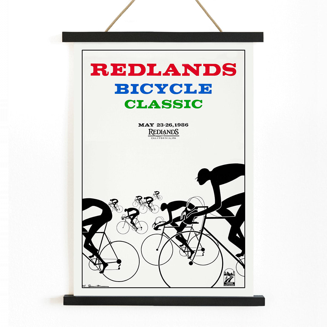 Cyclists racing illustration and poster by Karlis Smiltens titled Redlands Bicycle Classic featuring red blue and green text on white background, with wooden magnetic frame on white background