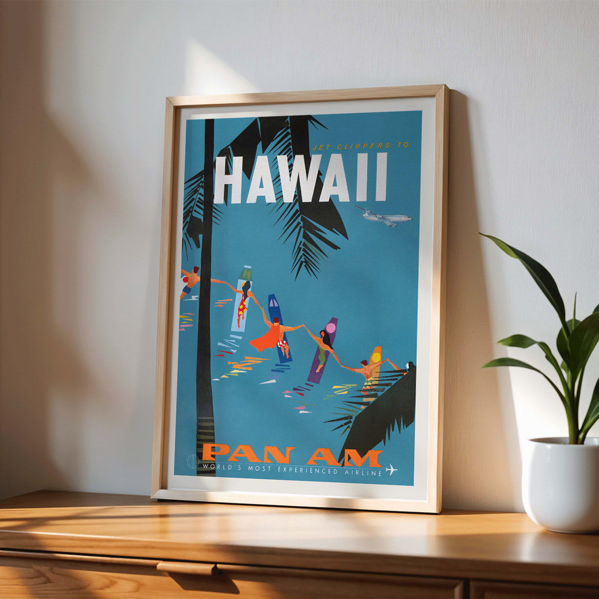 Colorful travel poster Jet Clipper to Hawaii by Pan Am Airlines with palm trees surfers dancers on surfboards and airplane above palm leaves, framed and displayed in modern living room decor