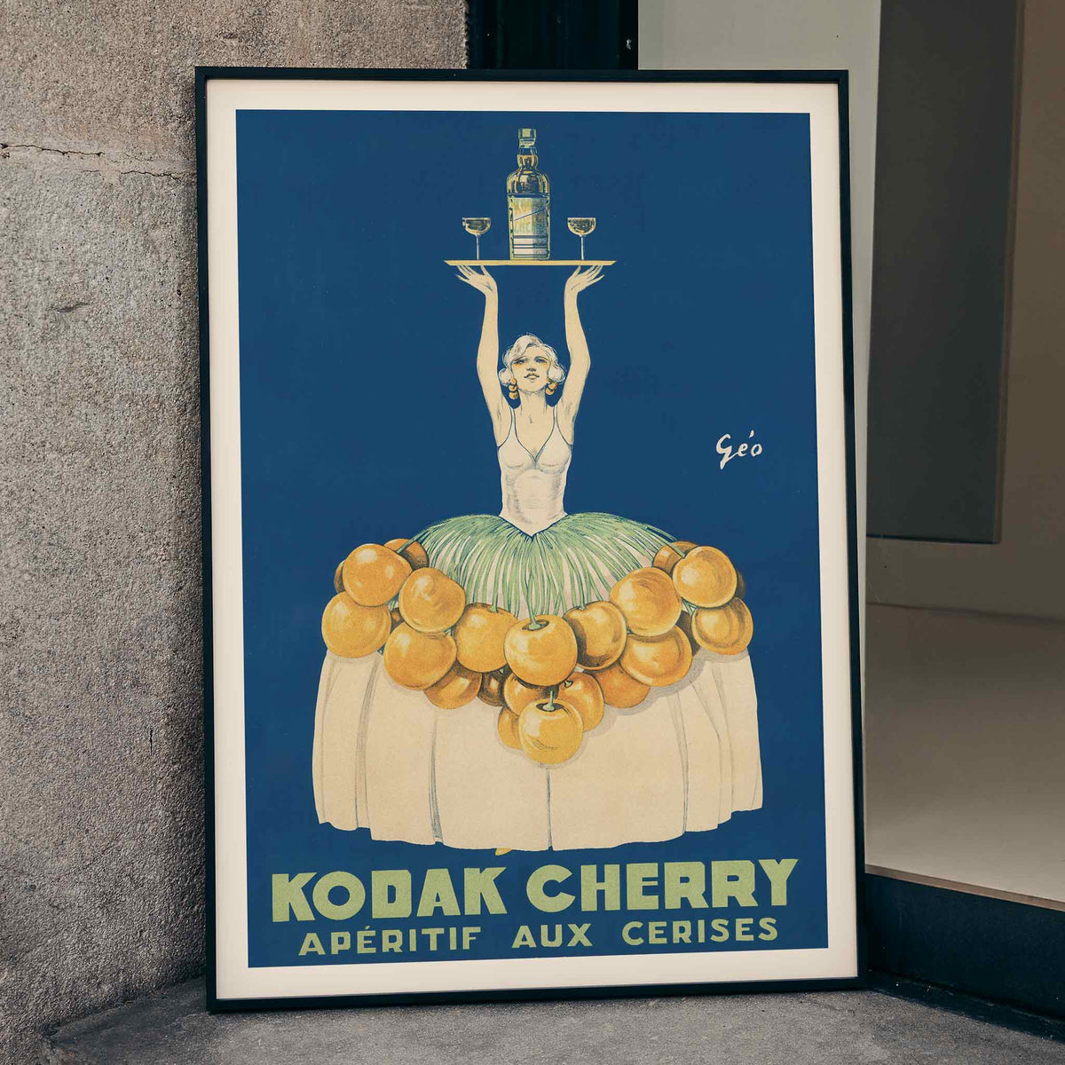 Géo Vermeire Kodak Cherry poster with woman in cherry-covered dress holding tray with bottle and two glasses, framed and displayed in home decor