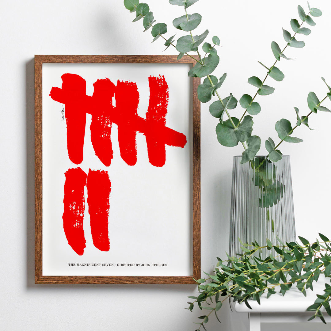 Minimalist movie poster for The Magnificent Seven by Saul Bass with bold red brushstroke tally marks on white background, framed and displayed in home decor