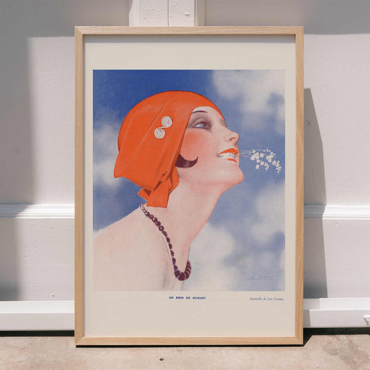 Poster of Un Brin de Muguet by Leo Fontan showing a smiling woman in a red headscarf holding lily of the valley in her mouth, framed and displayed in home decor