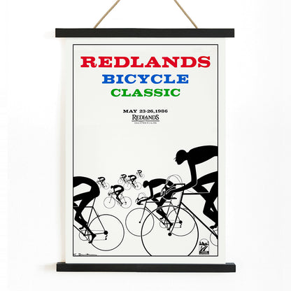 Cyclists racing illustration and poster by Karlis Smiltens titled Redlands Bicycle Classic featuring red blue and green text on white background, with wooden magnetic frame on white background
