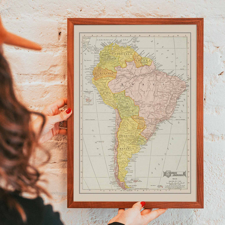 Vintage Rand McNally South America map poster with labeled continent in soft yellow pink and beige cartographic detail, framed and displayed in modern living room decor