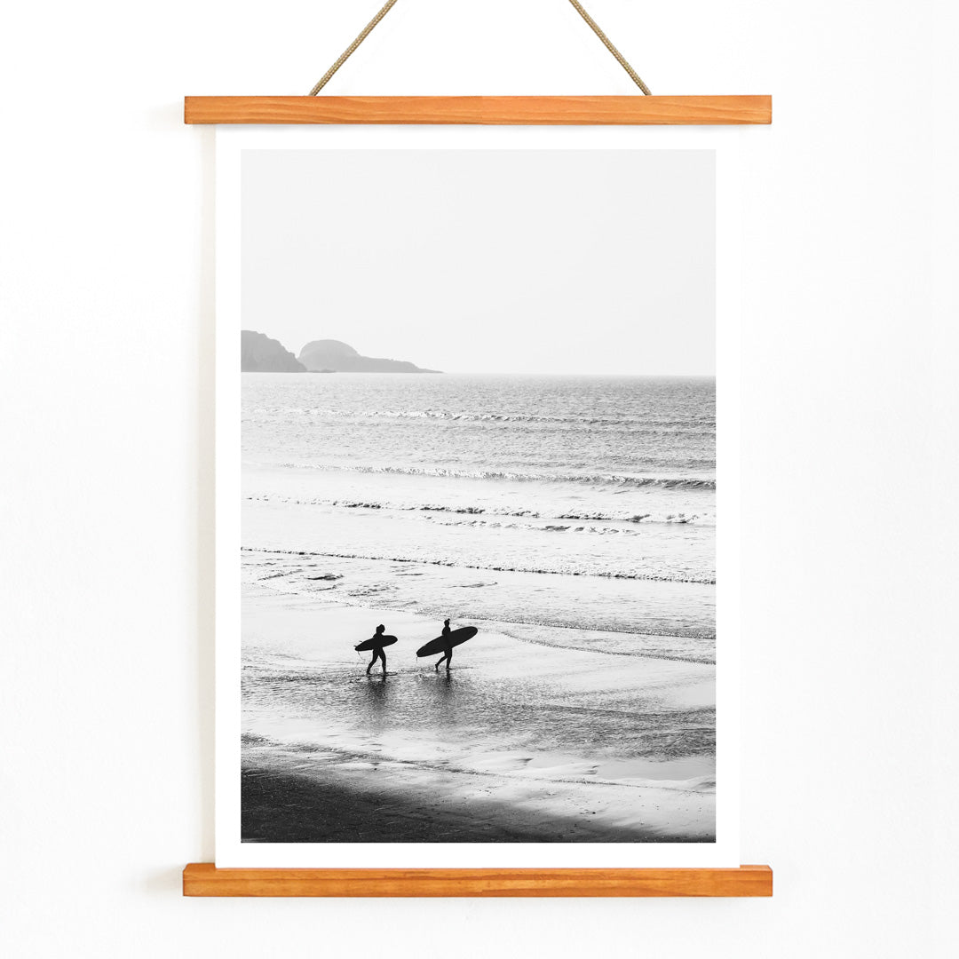 Black and white poster of surfers walking along the beach Surfers walking on the beach artwork, with wooden magnetic frame on white background