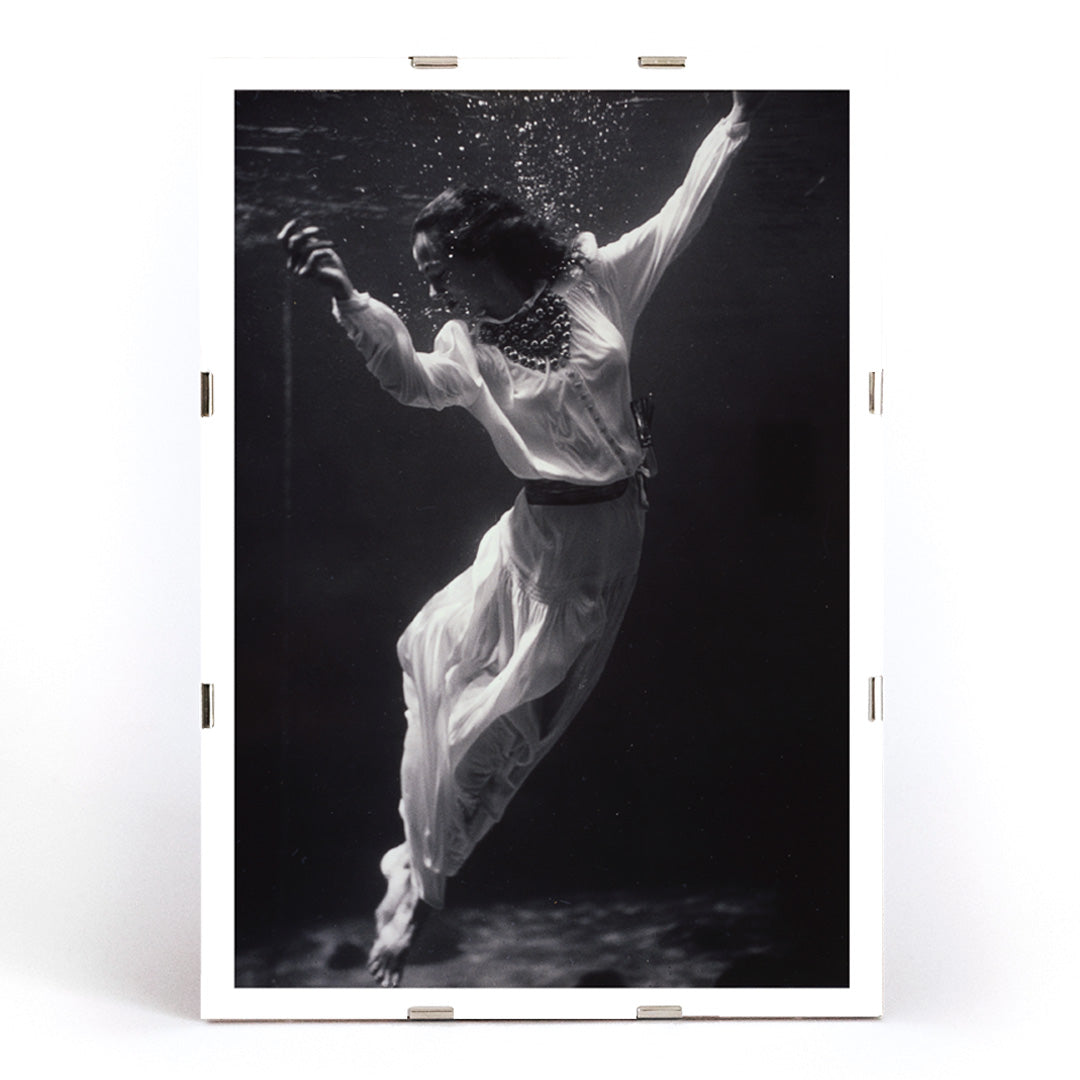 Black and white artwork of a fashion model floating underwater in dolphin tank Marineland Florida by Toni Frissell, framed and displayed in modern living room decor